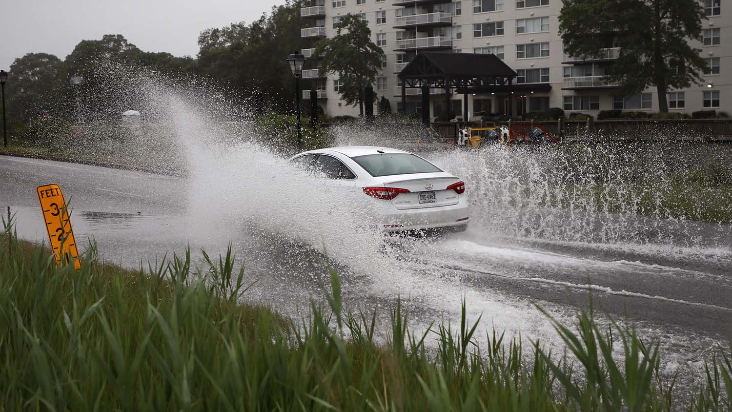 a car splashes through floodwaters on a roadway
