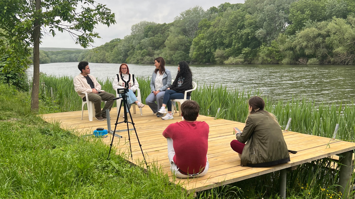 A group of people sitting on a small dock along a river.