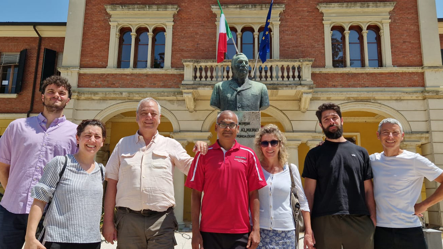 a group of people stand outside in front of a brick building and the bust of a man