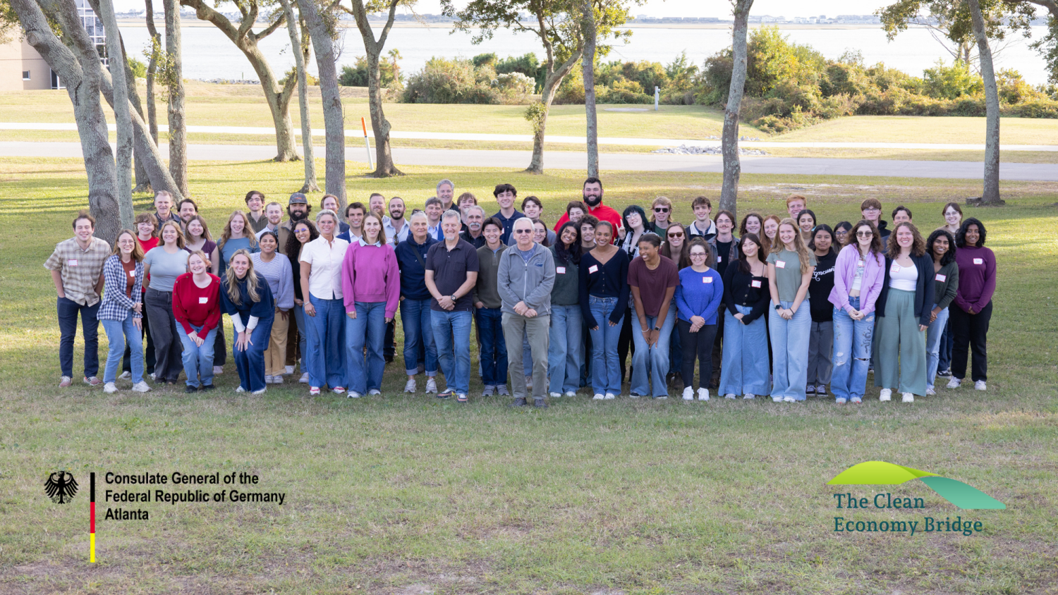 Group photo of 60+ attendees of the 2025 Blue Economy Innovation Workshop. The group stands on a grassy hill with the Bogue Sound in the background