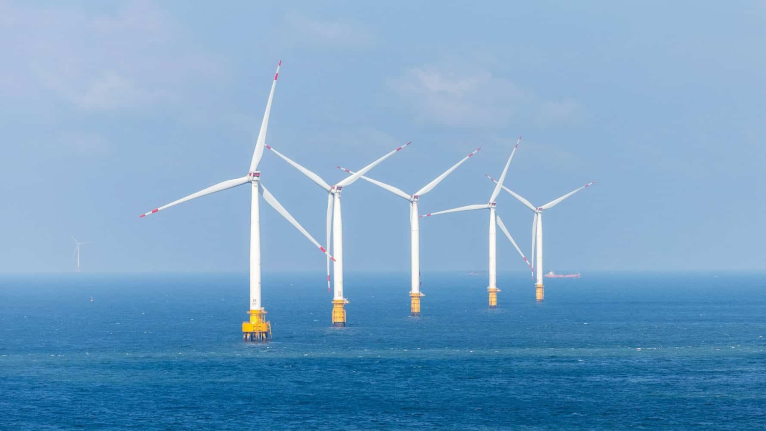 five large wind turbines stand in the ocean, with no land in sight
