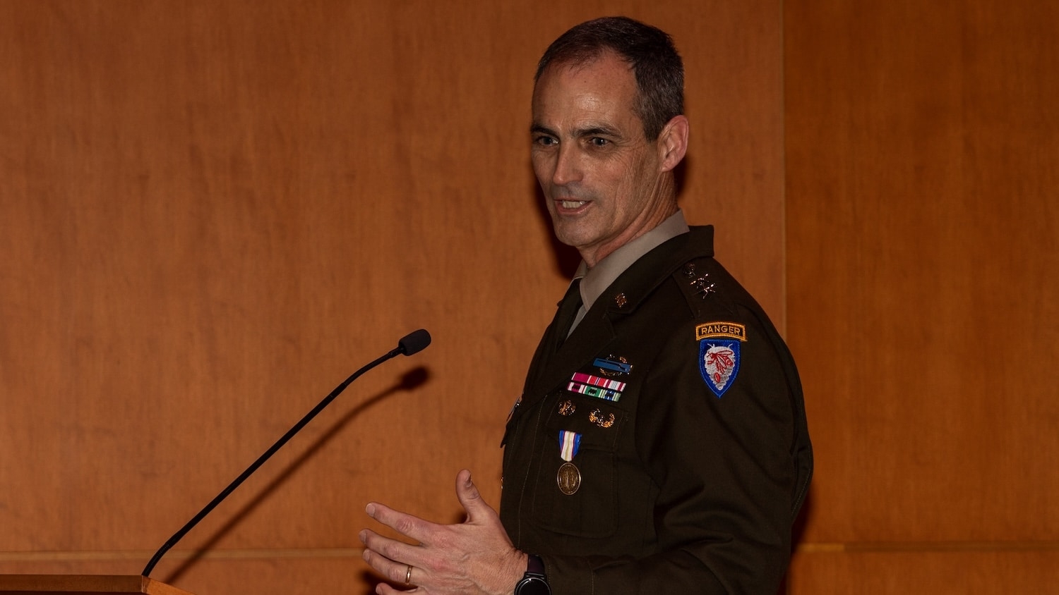 A man in a military uniform stands behind a microphone.