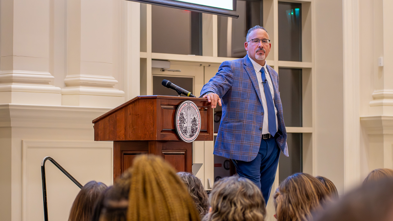 Former U.S. Secretary of Education Miguel Cardona stands beside a podium at the Park Alumni Center.