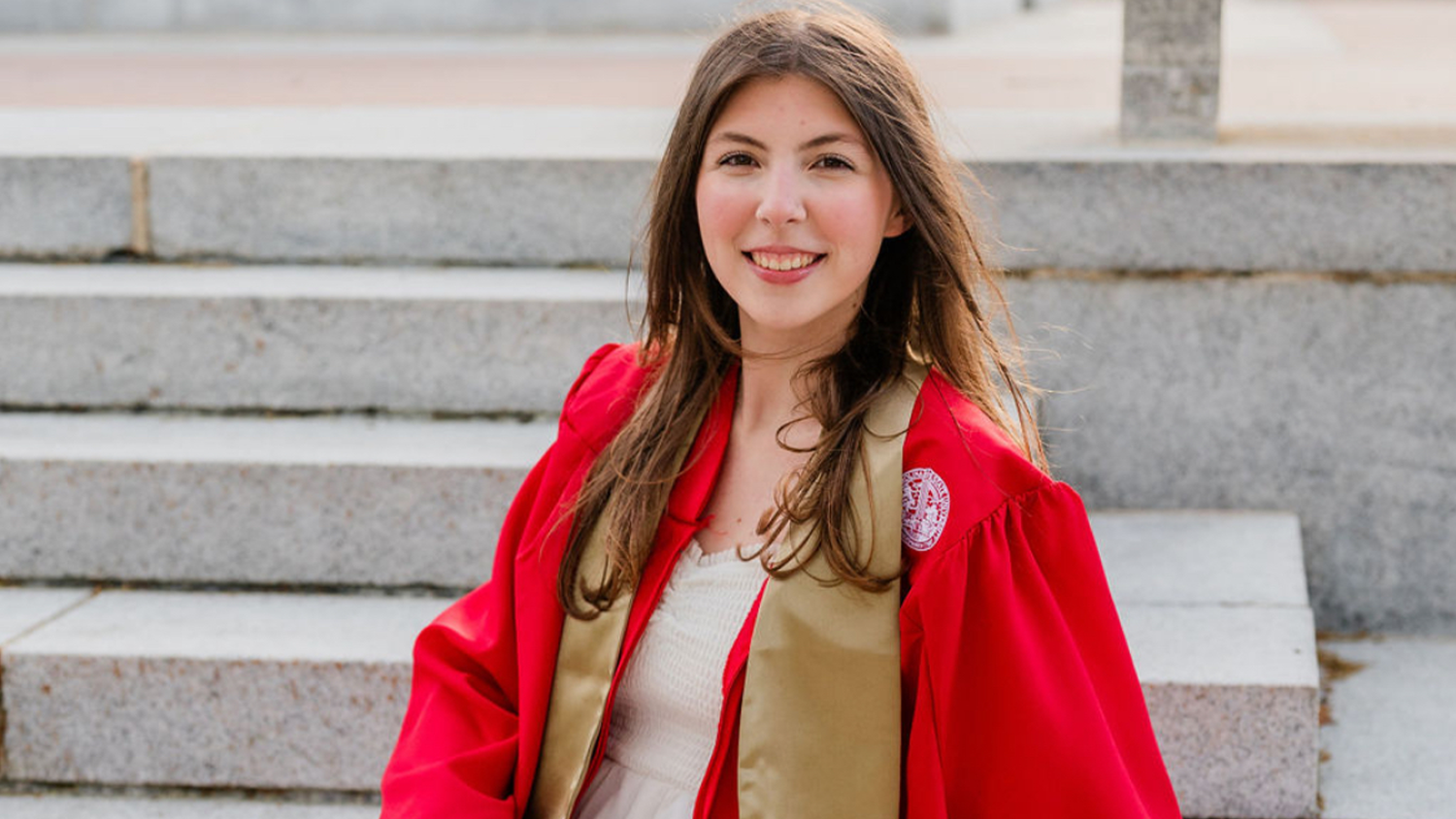 NC State alum Kelly Power sits on the steps of the Bell Tower in her graduation gown.