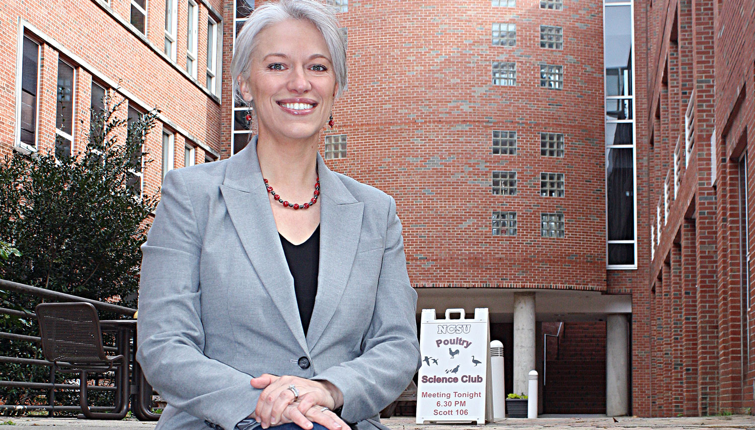 Summer Lanier next to a placard announcing a Poultry Science Club meeting in Scott Hall on the NC State University campus