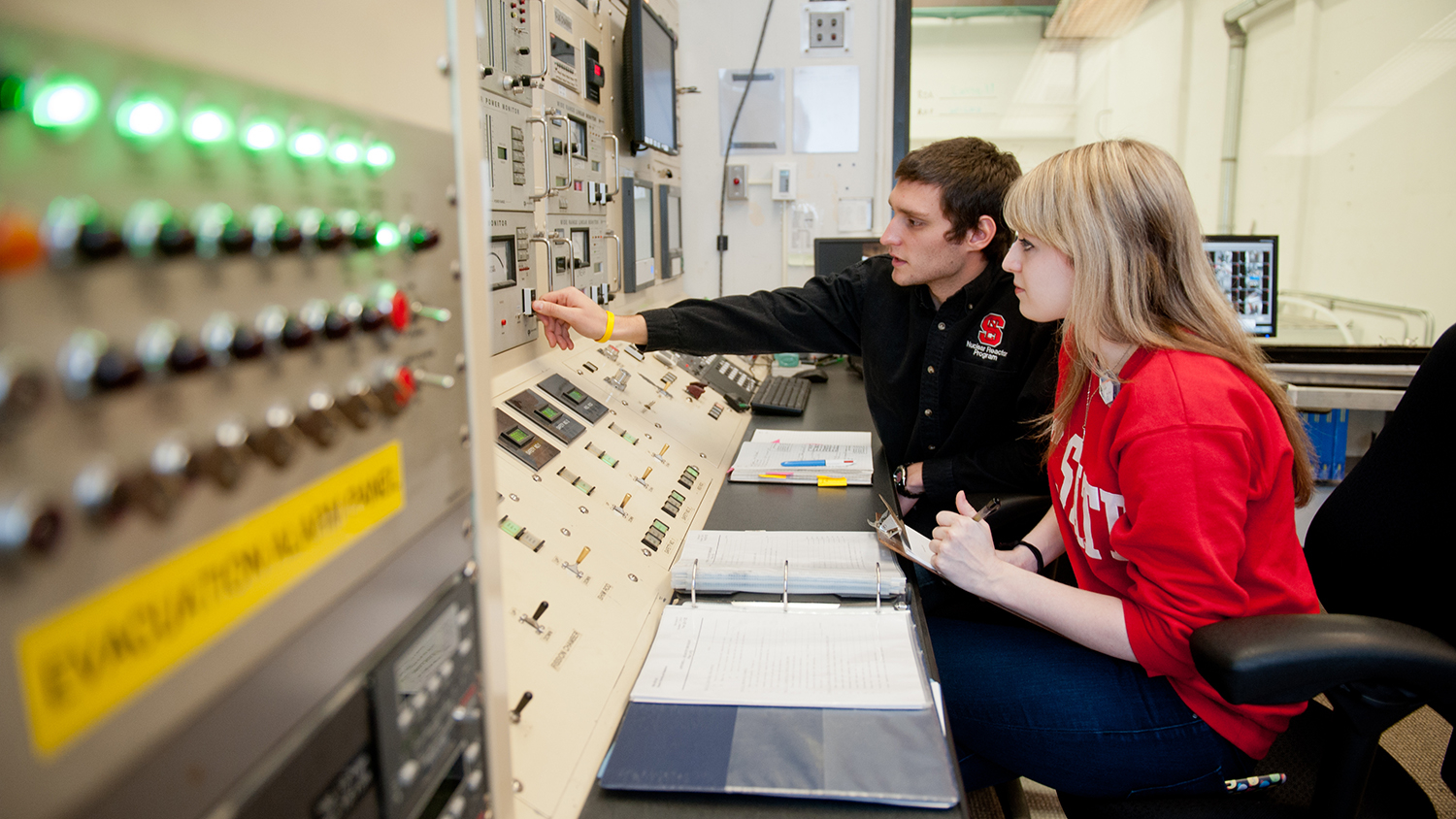 two engineering students sit at a nuclear research reactor control panel
