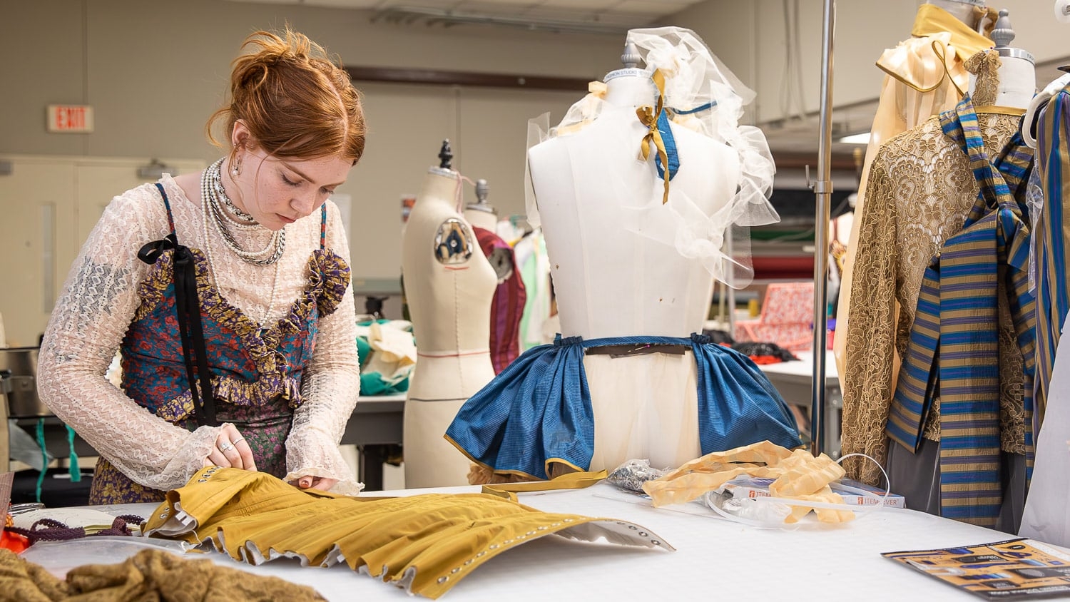A student stitches a garment with portions of the garment pinned onto a dressmaker's dummy beside her.