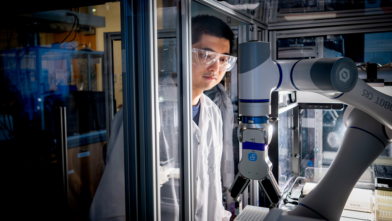 male researcher wearing protective eyewear observes a robotic arm in a self-driving lab