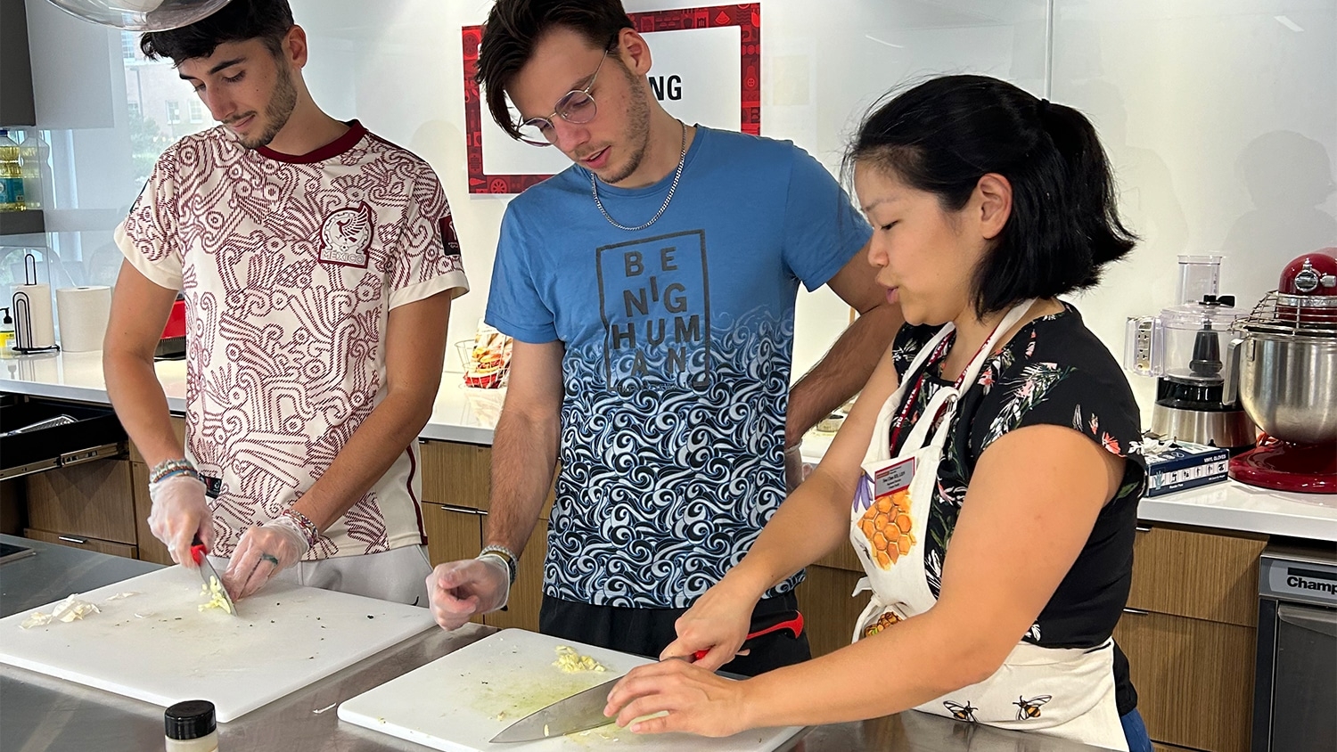 Soo Uhm demonstrates to two students how to chop an onion.