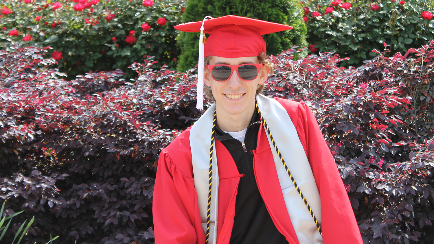 Trent Phillips wears his graduation cap, gown and a pair of sunglasses.
