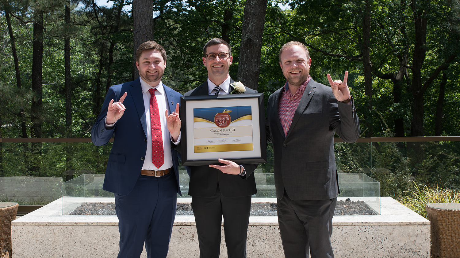 Teacher of the Year Cason Justice holds his award alongside two other men doing the wolfpack hand sign.