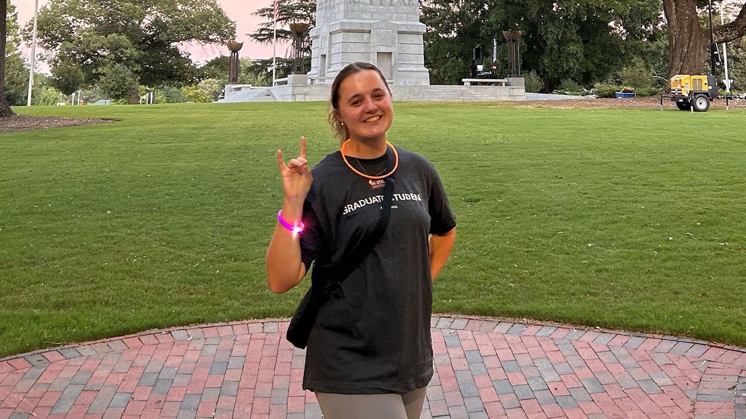 Grace Green does the wolfie hand sign while standing in front of the Bell Tower.