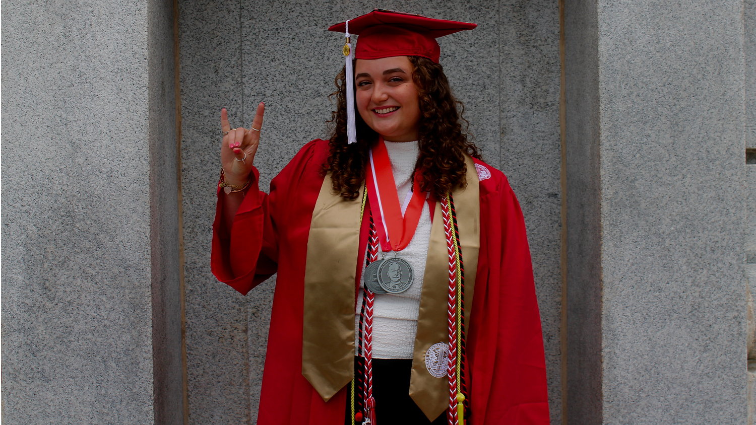 Molly Sue Smith wears her graduation cap and gown while giving the wolfie hand signal.