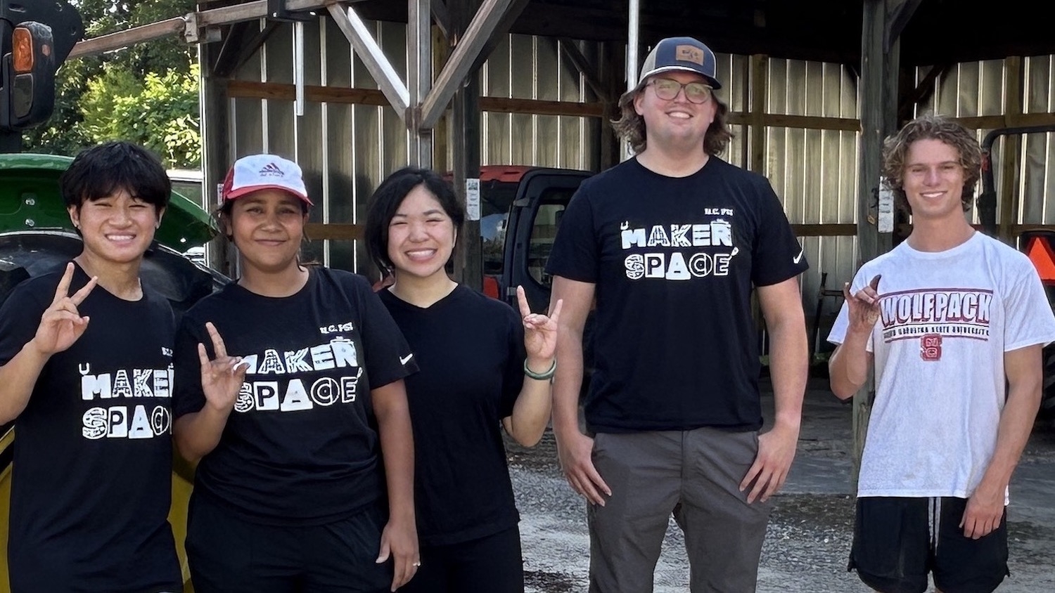 Five people pose near a work shed