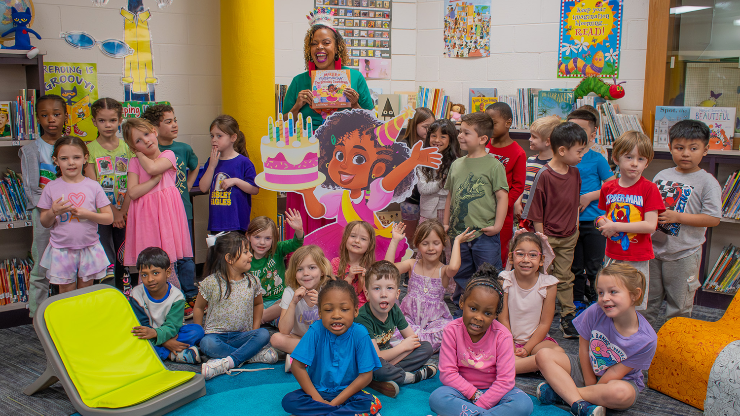 Marielle Myers ’07MED, ’14PHD hold her book while standing with a group of elementary school students inside a classroom.