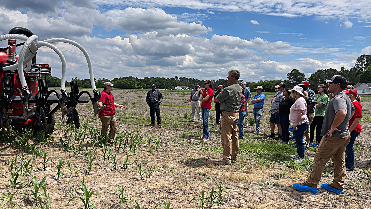 A woman speaks to a group during a workshop in a field.
