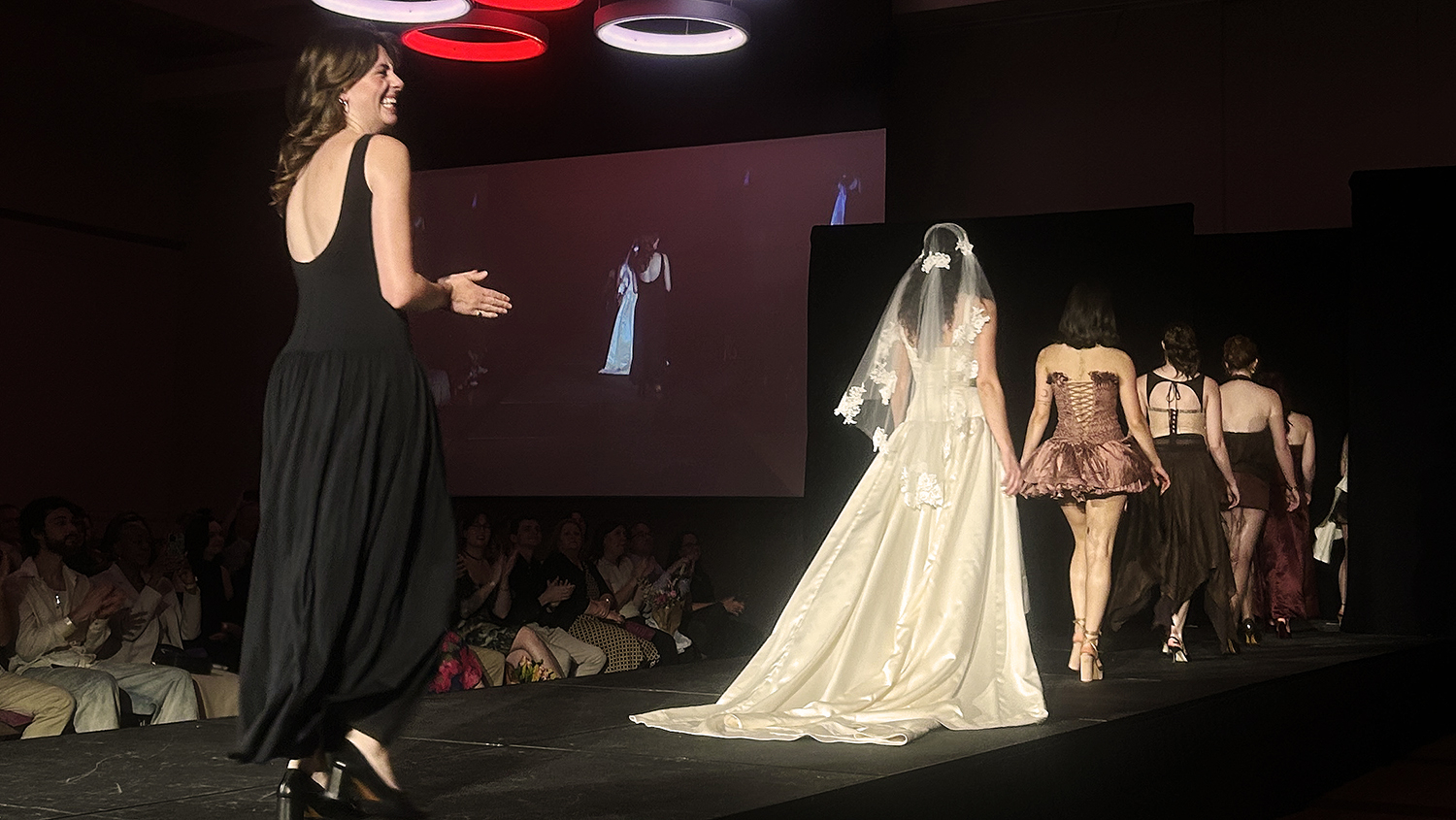 Julia Handley smiles and claps as she follows models off the runway. The last model is wearing a wedding gown.