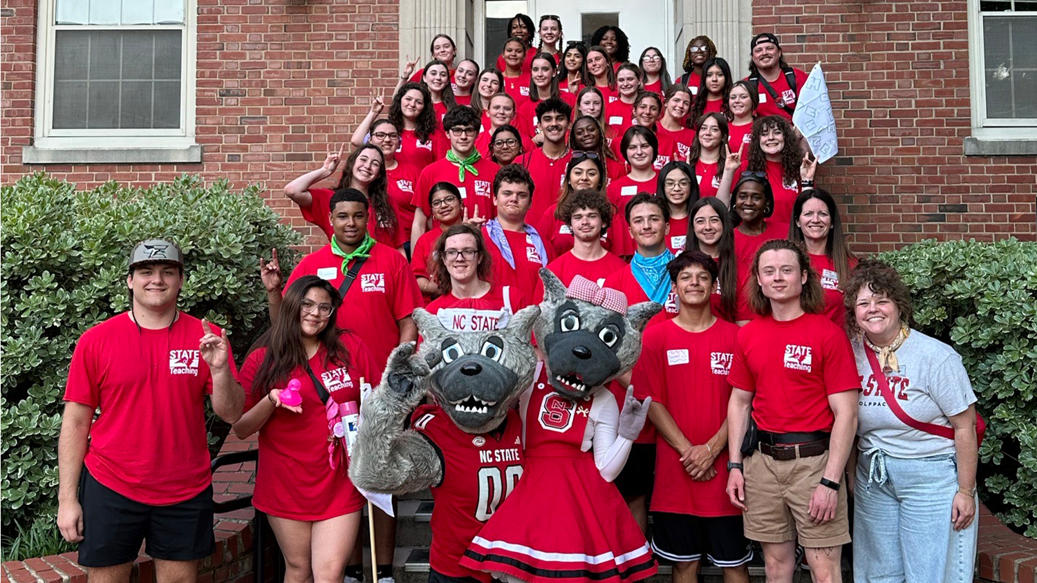 Students at the STATE of Teaching event pose for a group photo with Mr. and Ms. Wuf on the steps of a brick building.