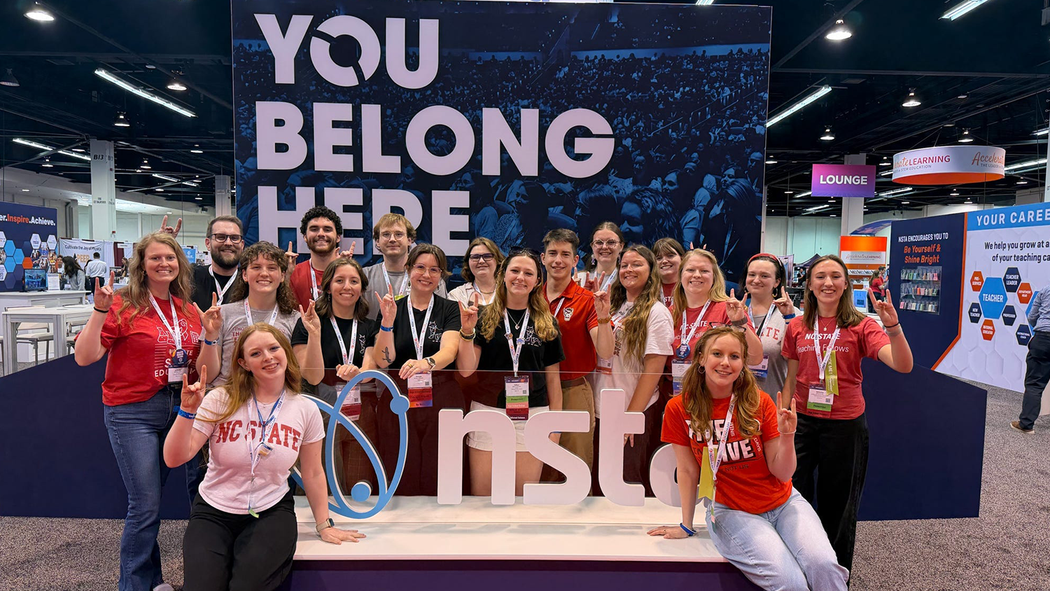 A group of science education students stand as a group in front of an NSTA banner at the conference in California.