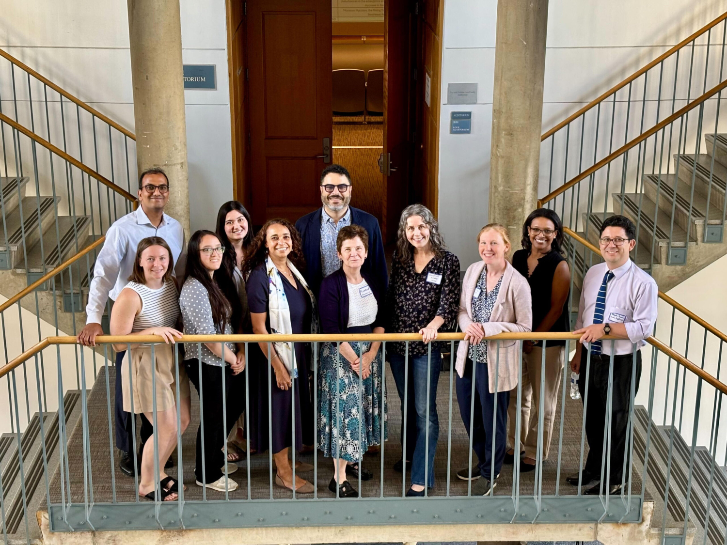The keynote speakers and symposium organizers smile and stand together in a staircase landing.