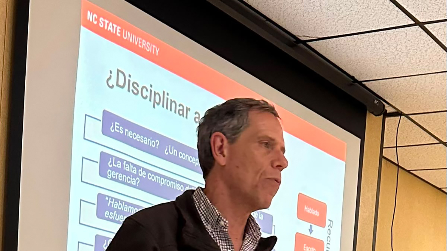 a man stands in front of a screen with Spanish language
