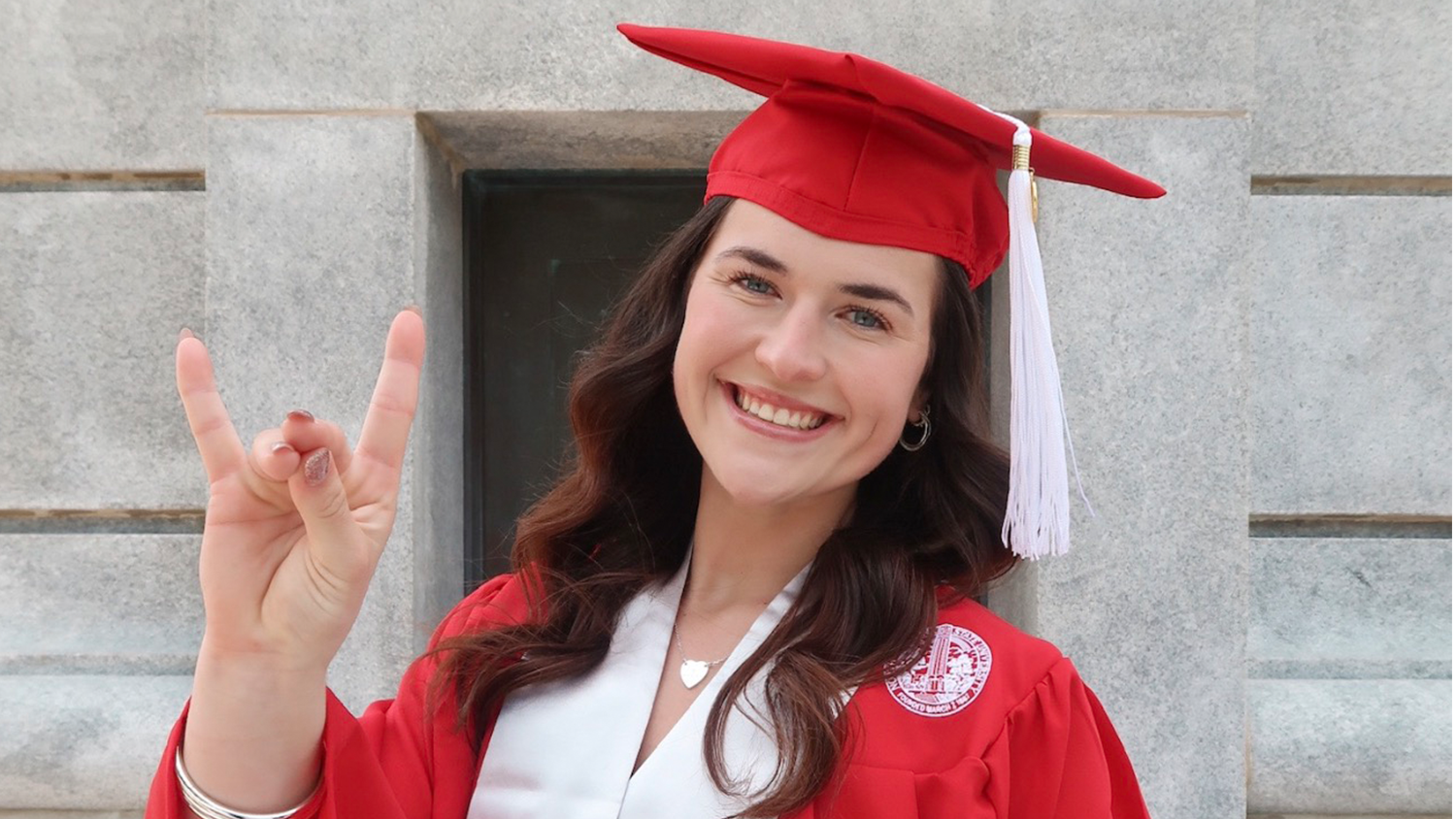 Avery Tucker wears her graduation cap and gown while doing the wolfie sign with her hand.
