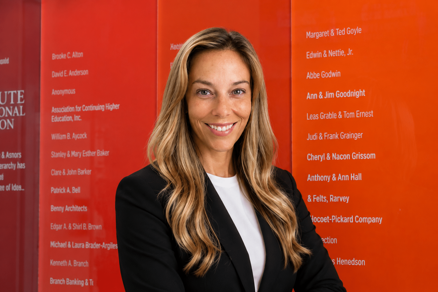 Headshot of Jessica Hunt, a woman with long blonde hair, black blazer and a red and orange striped background
