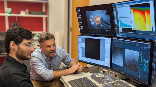 Two researchers sitting in front of four monitors in a research lab.