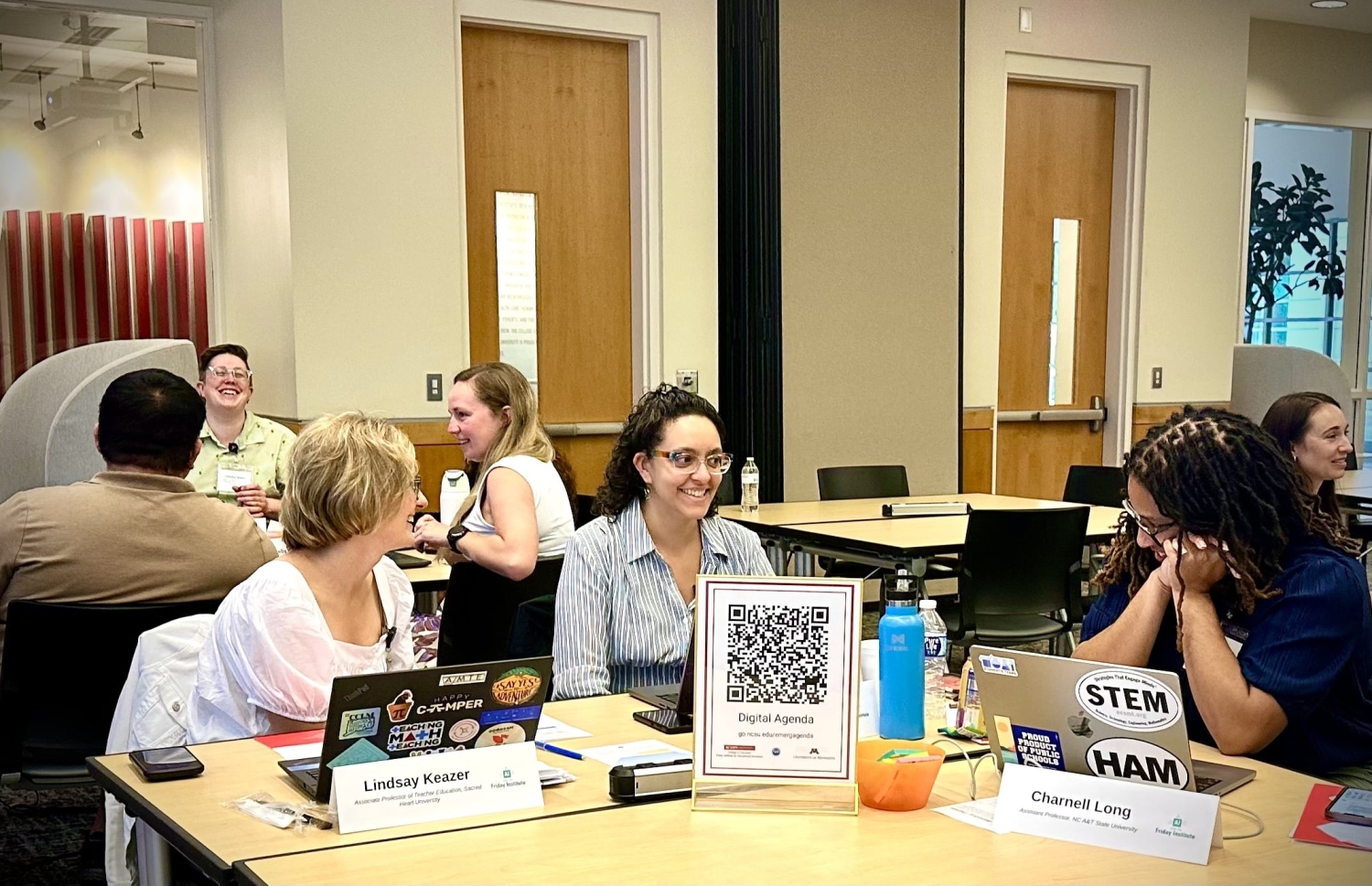 Three scholars sit smiling and having a conversation in a large meeting room