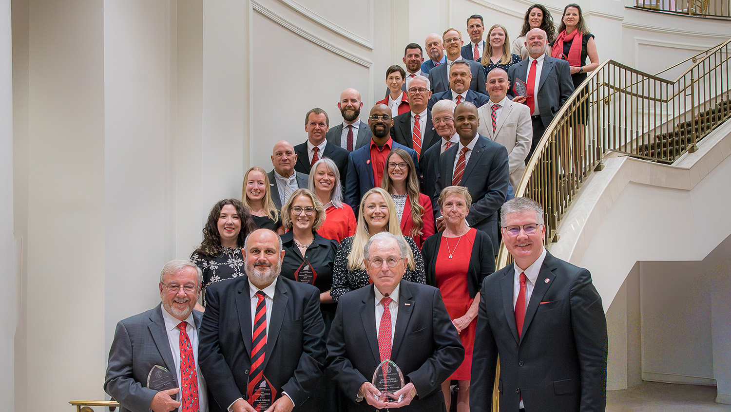 a group of 28 people stand on a staircase with a brass railing
