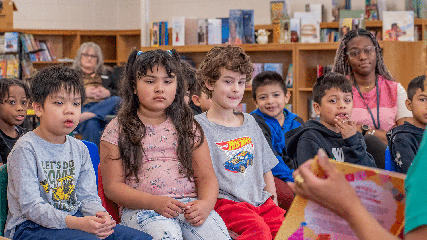A group of elementary school students sit and listen to a story in the school library.