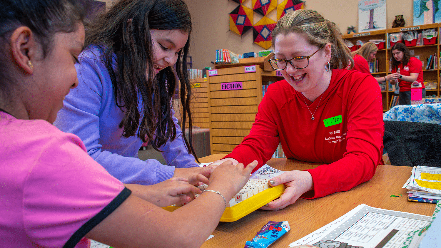 Two elementaryschoolers work at a table with a College of Education student.