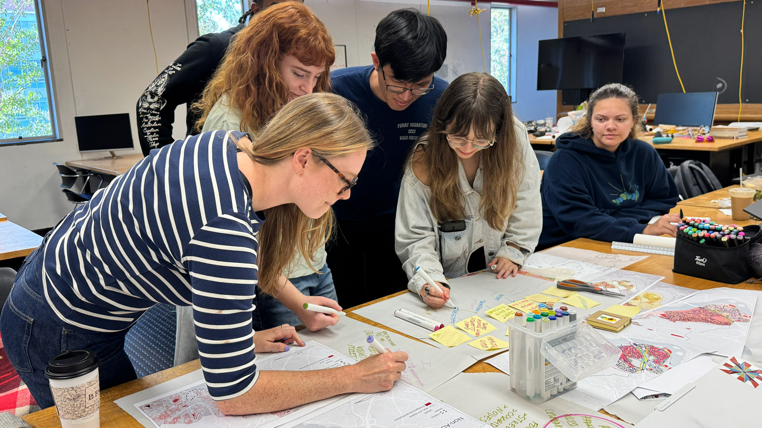 landscape architecture and architecture students lean over series of drawings to mark them up